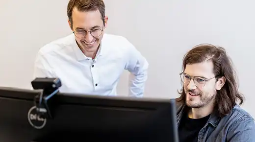 Two colleagues discuss something on a large screen in front of them