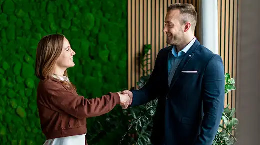 Two people shaking hands in a conference room with some greenery in the background