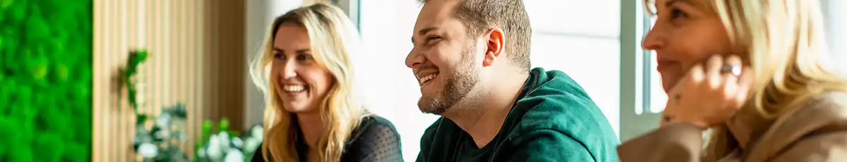 Three laughing colleagues in an office, talking to someone out of frame