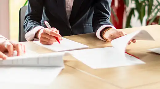 Documents spread on a table are being analyzed by a group of colleagues whose faces are cropped out of the image