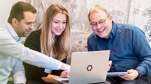 Team member shows something on a laptop to two other colleagues.