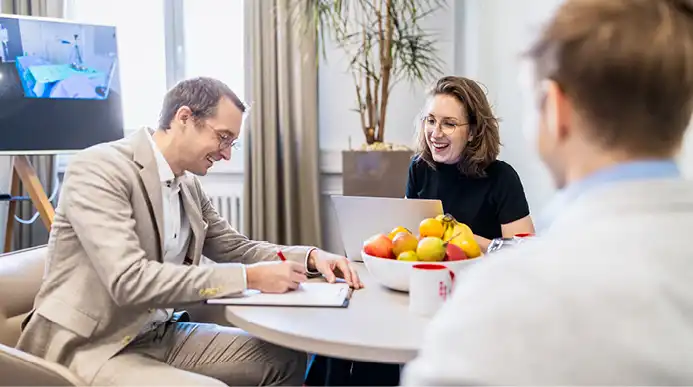 A small group of three employees seated at a table evaluate clients' results.