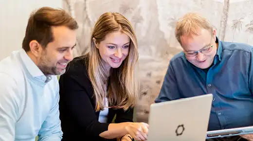 Three colleagues view something on a laptop.