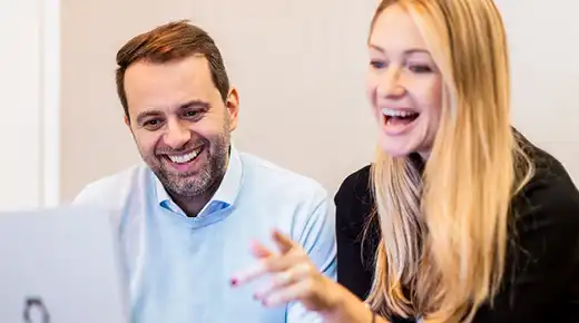 Two colleagues view something on a laptop while laughing.