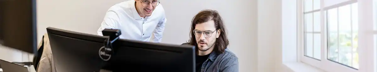 Two colleagues view something on a large desktop screen
