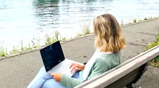 Woman sitting at the shores of Lake Constance with her laptop.