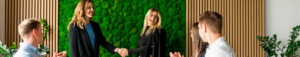 Two people shake hands in a gesture of agreement; other people in the room applaud.