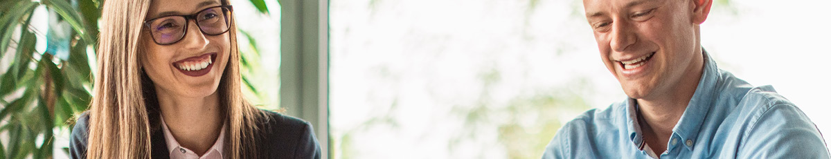 Two colleagues in an office setting are smiling.