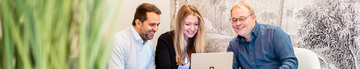 Three colleagues discuss something shown on their laptop screen.