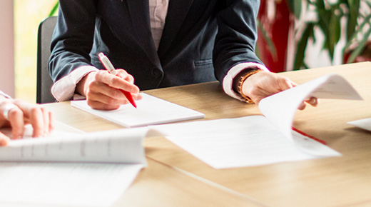 Documents spread on a table are being analyzed by a group of colleagues whose faces are cropped out of the image