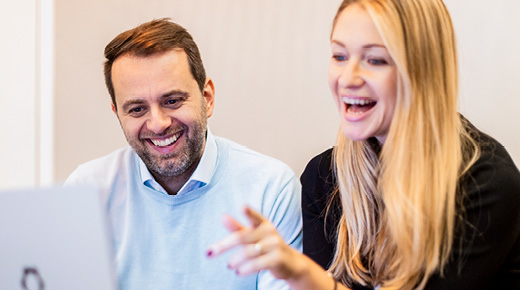 Two colleagues view something on a laptop while laughing.