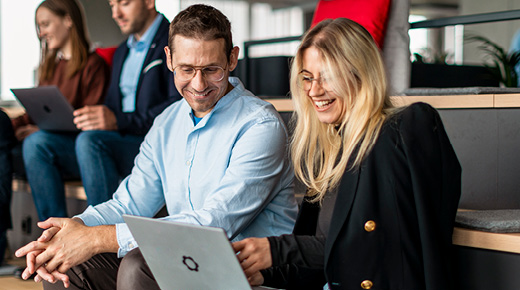 Colleagues sitting in a co-working space, chatting & discussing something on a laptop.