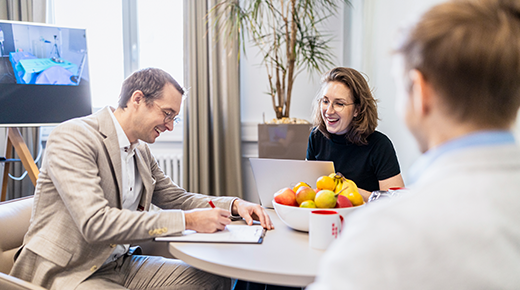 A small group of three employees seated at a table evaluate clients' results.